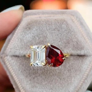 Peut inclure: Une bague en or avec une pierre rouge en forme de poire et une pierre transparente de forme carrée. La bague est dans un écrin à bague en velours gris.