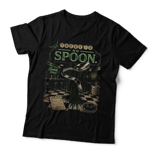 May include: A black short-sleeved t-shirt featuring a graphic print of a bent spoon floating above a chequered floor in a diner setting. The text "THERE IS NO SPOON." appears in green and white lettering above the spoon illustration.