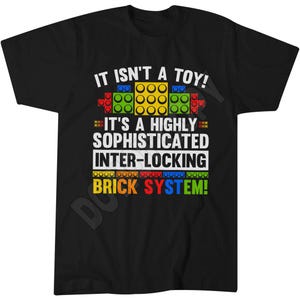 May include: A black short-sleeved t-shirt featuring a graphic with colourful plastic building blocks and the text: IT ISN'T A TOY! IT'S A HIGHLY SOPHISTICATED INTER-LOCKING BRICK SYSTEM! The design uses yellow, green, red, and blue block elements.