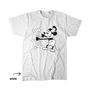 May include: A white short-sleeved t-shirt featuring a black and white graphic print of a cartoon mouse wearing a hat and steering a ship wheel. The design is centred on the chest area of the garment, which has a crew neckline and short sleeves.