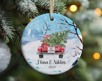 May include: A red truck with a Christmas tree in the back, driving through a snowy winter scene. The truck has a "Just Married" sign on the back. The ornament also includes the names "Elena & Niklas" and the year "2023".