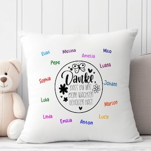 May include: White pillow with black text that reads "Danke, dass du uns beim wachsen geholfen hast" surrounded by a circle with a butterfly and flowers. The names Elias, Pepe, Sophia, Luka, Melina, Amelia, Milo, Luana, Johann, Marlon, Linda, Lucy, Emilia, and Anton are written around the circle in different colors.