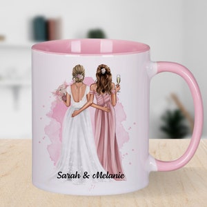 Könnte beinhalten: Weiße Keramiktasse mit rosafarbenem Rand und Henkel. Die Tasse zeigt eine Aquarell-Illustration von zwei Frauen in Hochzeitskleidung, eine in einem weißen Kleid und die andere in einem rosafarbenen Kleid. Der Text "Sarah & Melanie" ist unter der Illustration gedruckt.