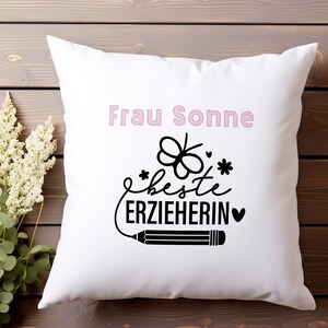 May include: White pillow with pink text that says "Frau Sonne" and black text that says "Beste Erzieherin" with a small heart and a pencil drawing.