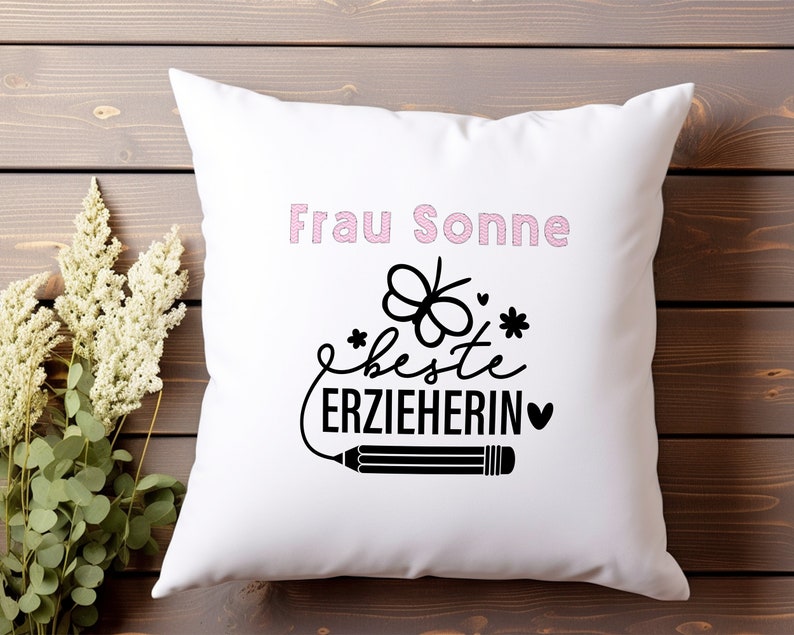 May include: White pillow with pink text that says "Frau Sonne" and black text that says "Beste Erzieherin" with a small heart and a pencil drawing.