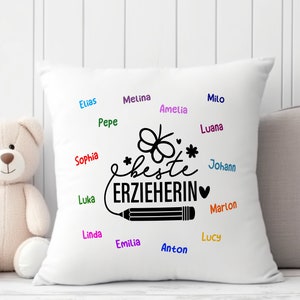 May include: White pillow with black text that says "*beste ERZIEHERIN*" with a pencil and a butterfly design. The pillow is surrounded by names written in different colors.