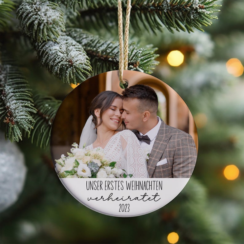 K&ouml;nnte beinhalten: Ein runder wei&szlig;er Weihnachtsbaumschmuck mit einem Foto eines Paares in Hochzeitskleidung. Der Anh&auml;nger hat den Text "Unser erstes Weihnachten verheiratet 2023" aufgedruckt.