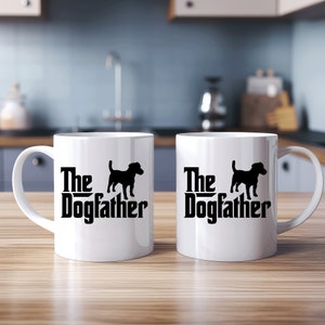 Könnte beinhalten: Zwei weiße Keramikbecher mit schwarzen Henkeln. Jeder Becher hat eine schwarze Silhouette eines Hundes und den Text "The Dogfather" auf der Vorderseite.