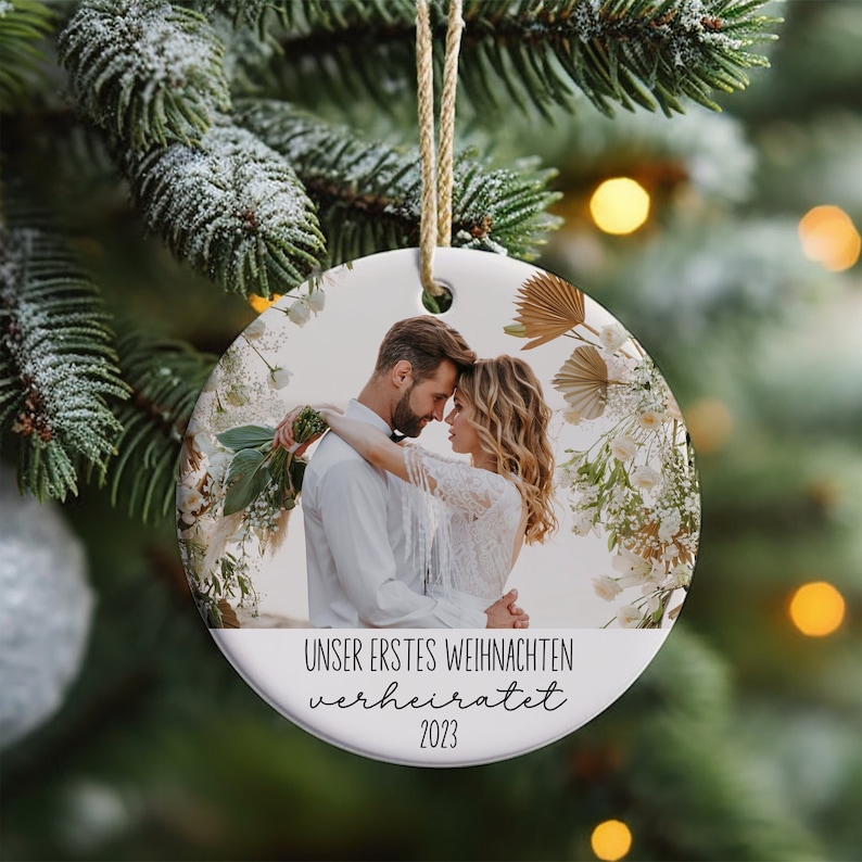 K&ouml;nnte beinhalten: Ein runder wei&szlig;er Keramik-Anh&auml;nger mit einem Foto eines Paares vor einem floralen Hintergrund. Der Text "Unser erstes Weihnachten verheiratet 2023" ist auf dem Anh&auml;nger gedruckt.