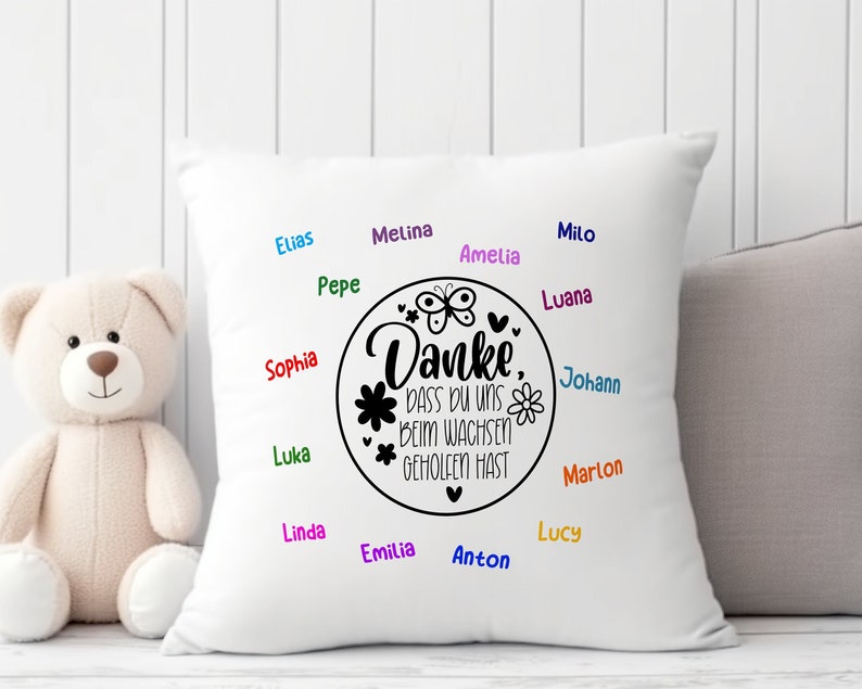 May include: White pillow with black text that reads "Danke, dass du uns beim wachsen geholfen hast" surrounded by a circle with a butterfly and flowers. The names Elias, Pepe, Sophia, Luka, Melina, Amelia, Milo, Luana, Johann, Marlon, Linda, Lucy, Emilia, and Anton are written around the circle in different colors.