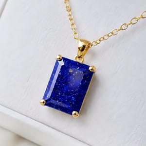 Pode incluir: Um colar de ouro com um pendente retangular de lápis-lazúli facetado. A pedra azul profunda apresenta manchas naturais de cor dourada e é fixada por quatro garras de ouro. O pendente está suspenso numa delicada corrente de ouro com elos circulares.