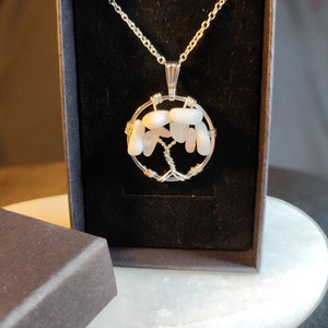 Peut inclure: Un collier en chaîne argent avec un pendentif enroulé de fil représentant un arbre en pierres roses et blanches.