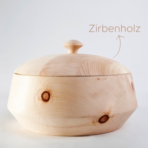 Könnte beinhalten: Eine Brotbox aus Holz mit einem Deckel aus Zirbenholz. Die Box ist hellbraun und hat eine natürliche Holzoptik. Der Text "Zirbenholz" ist auf dem Bild zu sehen.