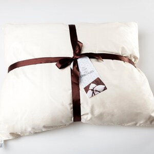 May include: A white pillow tied with a brown ribbon and a tag that says "ZIRBELZAUBER".