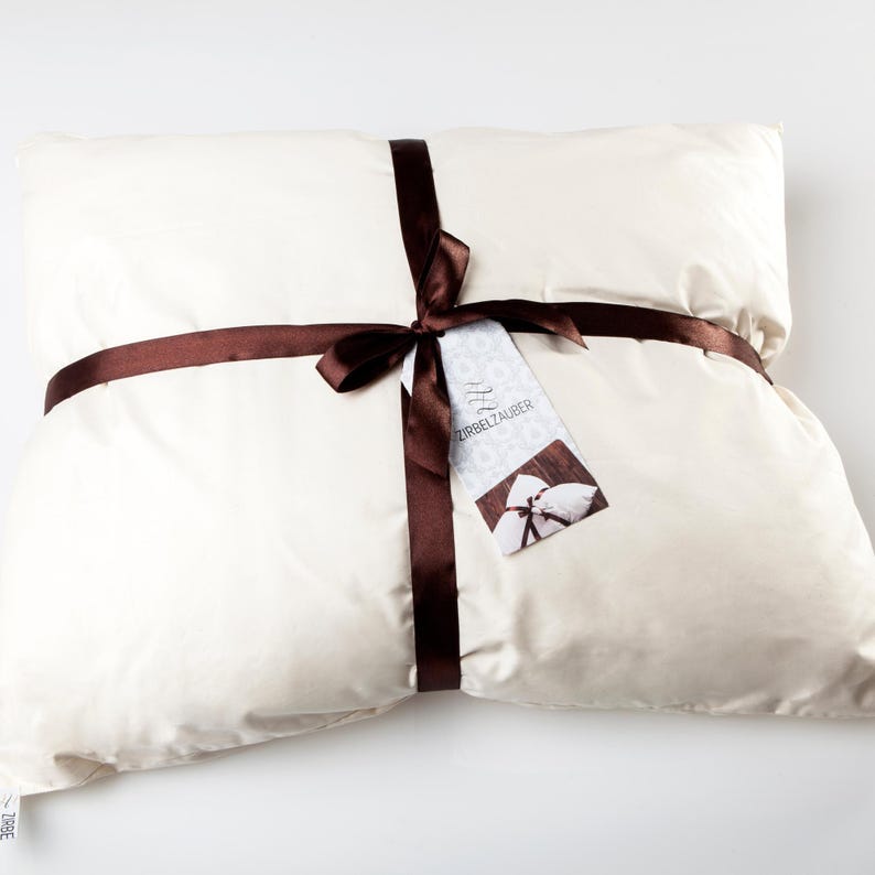 May include: A white pillow tied with a brown ribbon and a tag that says "ZIRBELZAUBER".