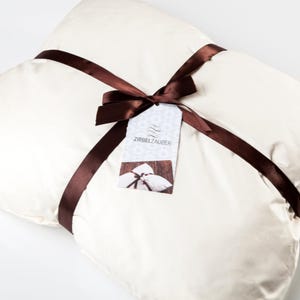 May include: A white pillow tied with a brown ribbon and a gift tag that says "Zirbelzauber".