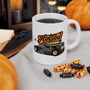 May include: White ceramic mug with a hotrod illustration and the text "Hotrod Outlaw & Garage". The mug is filled with coffee and steam is rising from the top.