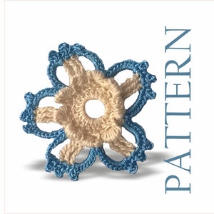 以下が含まれることがあります： 薄い青色の外縁とベージュの中心を持つ、かぎ針編みの花。花は5枚の花びらと中心に穴があります。