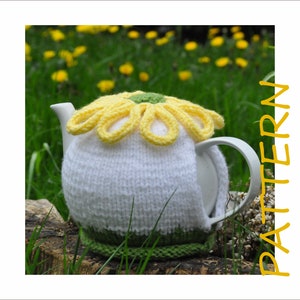 Könnte beinhalten: Ein weißer gestrickter Teekannenwärmer mit einem gelben Gänseblümchen-Blütenmuster. Der Wärmer befindet sich auf einer Teekanne mit weißem Hintergrund und grünem Sockel. Die Teekanne steht auf einem Baumstumpf in einem Feld mit grünem Gras und gelben Blumen.