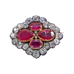 May include: A vintage brooch featuring four oval-cut rubies set in gold, surrounded by numerous clear, sparkling diamonds. The brooch has a rectangular shape with a pin closure on the back, perfect for adding a touch of elegance to any outfit.