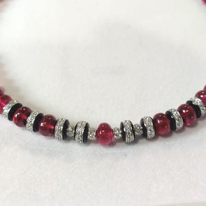 Pode incluir: Um colar com contas vermelhas alternadas e espa&ccedil;adores prateados com cristais transparentes. O colar tem um tom vermelho escuro e &eacute; exibido em uma superf&iacute;cie branca. As contas t&ecirc;m aproximadamente 1,3 cm de di&acirc;metro.