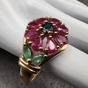 May include: A gold ring with a ruby and emerald flower design. The center of the flower has a black gemstone.