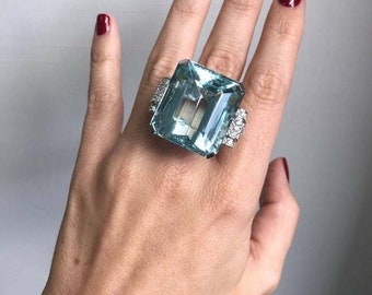 May include: A large, light blue aquamarine gemstone ring set in a silver band with smaller diamonds surrounding the main stone.