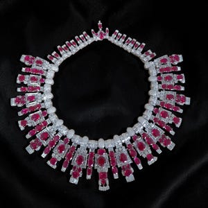 Op de afbeelding: Een luxe ketting met een schitterende reeks rode edelstenen en sprankelende witte diamanten. De ketting is gezet in een zilveren of witgouden zetting, met een symmetrisch ontwerp. De edelstenen zijn een levendige rode kleur en de diamanten voegen schittering toe.