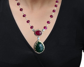 May include: A statement necklace with a two-tiered pendant featuring carved green and red gemstones surrounded by sparkling diamonds. The necklace is made of a string of pink beads.