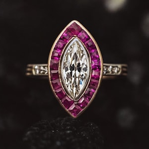 Puede incluir: Un anillo de diamantes de talla marquesa con un halo de rubíes rosas y una banda de diamantes más pequeños.