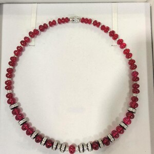Pode incluir: Um colar de contas vermelhas com detalhes em prata e diamantes. O colar &eacute; composto por contas vermelhas polidas, com se&ccedil;&otilde;es de espa&ccedil;adores prateados cravejados com diamantes. O fecho &eacute; prateado e tem um design de diamante.