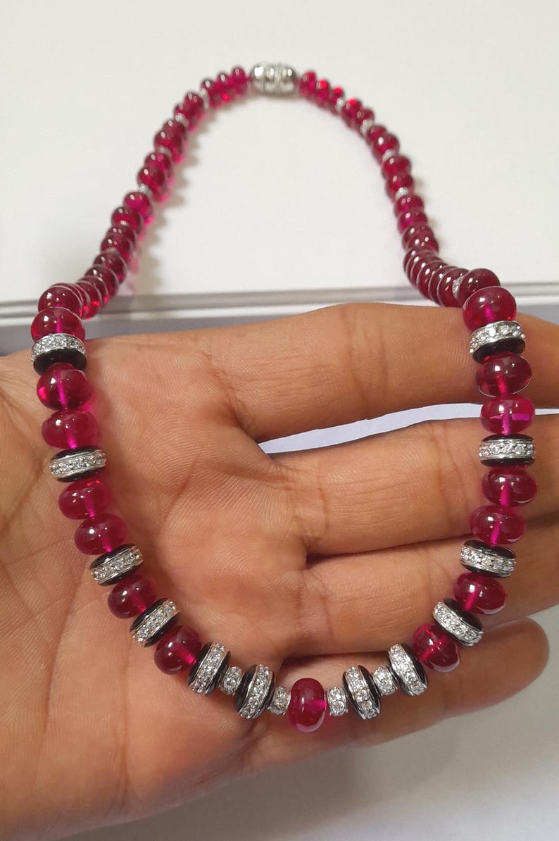 Pode incluir: Um colar com contas vermelho rubi alternadas e se&ccedil;&otilde;es com detalhes prateados e pedras transparentes. O colar tem um fecho prateado. As contas s&atilde;o de cor vermelha profunda.