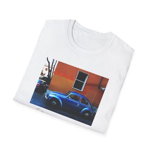 Può includere: T-shirt bianco con una fotografia di un'auto blu d'epoca parcheggiata di fronte a un edificio arancione con una finestra. L'immagine mette in risalto l'auto.