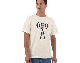 May include: A cream-colored short-sleeve t-shirt featuring a black graphic print of a radio tower. At the top of the tower is a smiling person's head with a pipe, surrounded by curved lines representing radio waves emanating from the center.