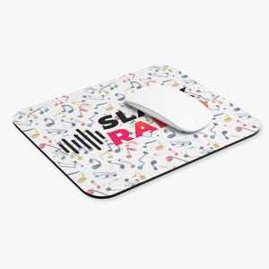 May include: Rectangular mousepad with a white background covered in colorful musical notes. The mousepad has the words "SL RA" in black and pink, with a graphic of sound waves. A white computer mouse is on the mousepad.