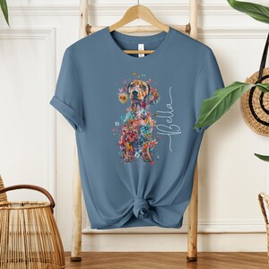 Op de afbeelding: Een blauw t-shirt met een bloemig teckelontwerp en de naam "Bella" in wit gedrukt.