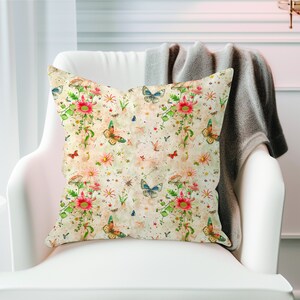 May include: A decorative throw pillow with a floral and butterfly pattern. The pillow features a light beige background with pink, red, green, blue, and yellow accents. The pattern includes butterflies, flowers, and mushrooms.