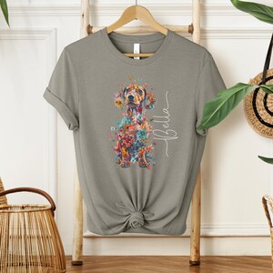 Op de afbeelding: Een grijs T-shirt met een bloemig teckelontwerp en de naam "Bella" in wit schrift.