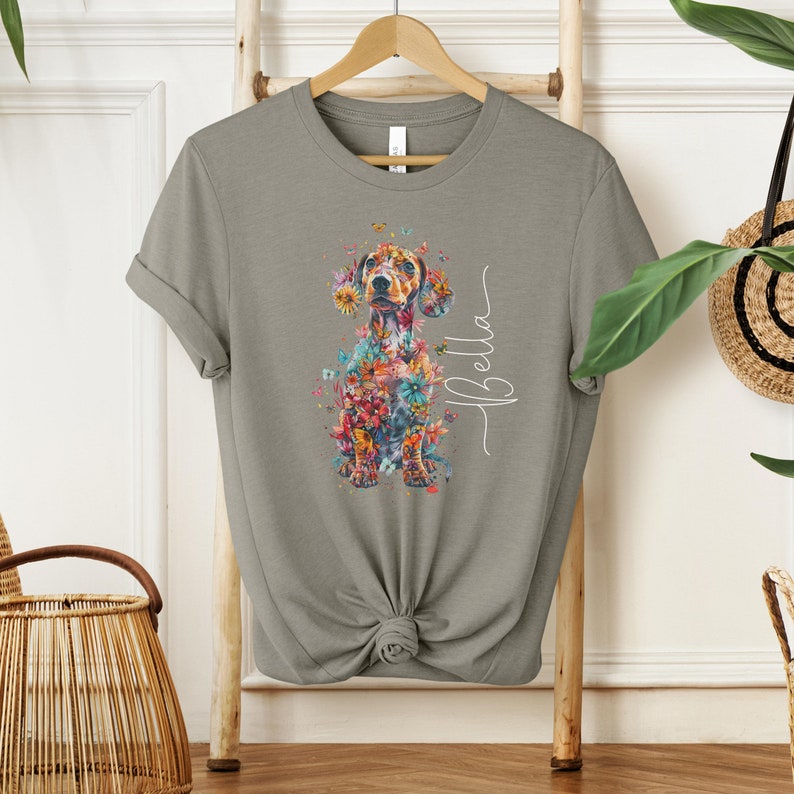 Op de afbeelding: Een grijs T-shirt met een bloemig teckelontwerp en de naam "Bella" in wit schrift.