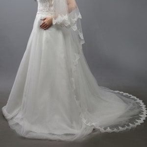 May include: A white wedding dress with a tulle skirt and lace trim. The dress has a sweetheart neckline and a fitted bodice. The bride is wearing a tiara and a veil.