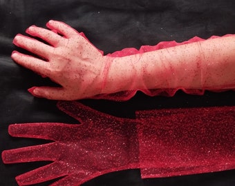 May include: A pair of red tulle gloves with glitter. One glove is on a hand, and the other is laid flat.