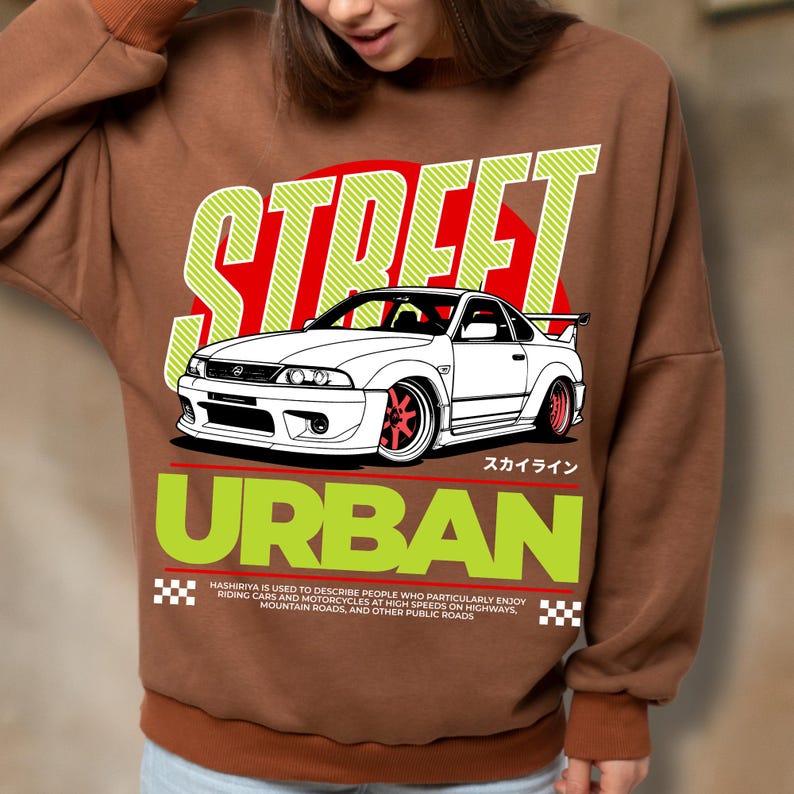 Puede incluir: Sudadera marr&oacute;n con un gr&aacute;fico de un coche deportivo blanco con ruedas rojas, sobre un c&iacute;rculo rojo y las palabras "STREET" y "URBAN" en verde. Tambi&eacute;n est&aacute; presente el texto "HASHIRIYA IS USED TO DESCRIBE PEOPLE WHO PARTICULARLY ENJOY RIDING CARS AND MOTORCYCLES AT HIGH SPEEDS ON HIGHWAYS, MOUNTAIN ROADS, AND OTHER PUBLIC ROADS".