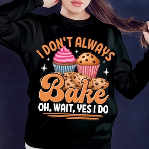 May include: Black sweatshirt featuring the text "I don't always bake, oh wait, yes I do." The design includes illustrations of cupcakes and cookies. A casual, comfortable style of clothing.