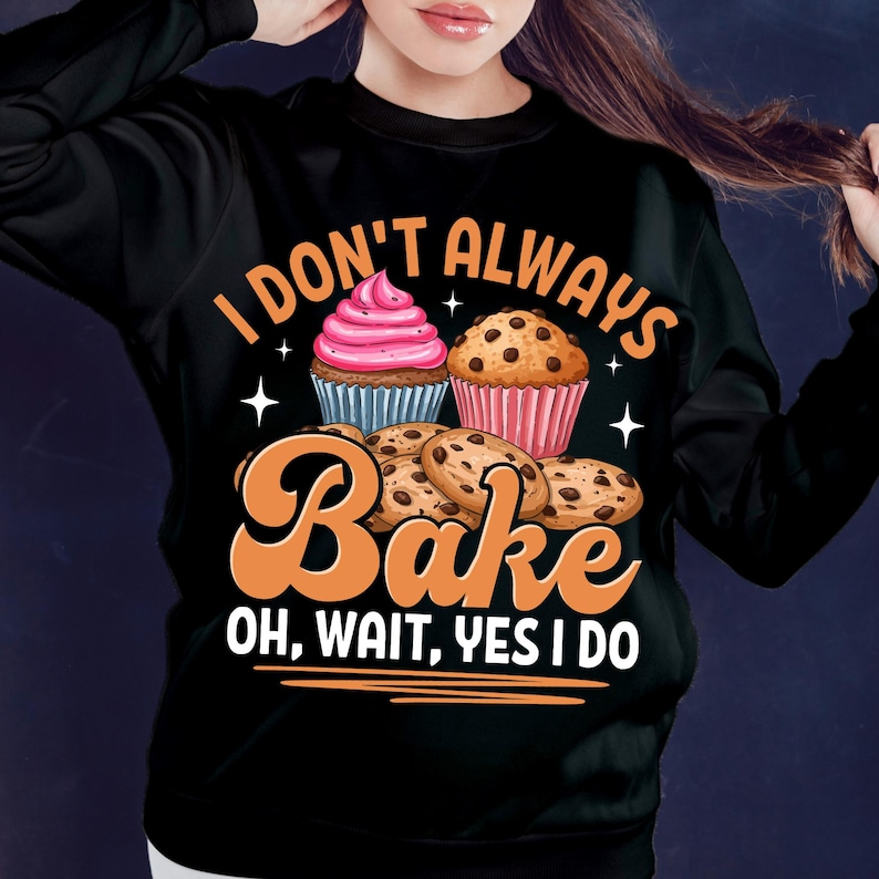 May include: Black sweatshirt featuring the text "I don't always bake, oh wait, yes I do." The design includes illustrations of cupcakes and cookies. A casual, comfortable style of clothing.