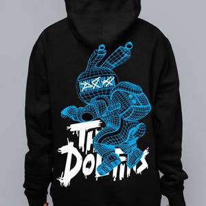May include: A black hooded sweatshirt featuring a blue wireframe graphic of a rabbit-like character with X-shaped eyes. Below the character, the text "THE DOLLINS" is printed in a distressed white font. The design is centered on the back of the garment.