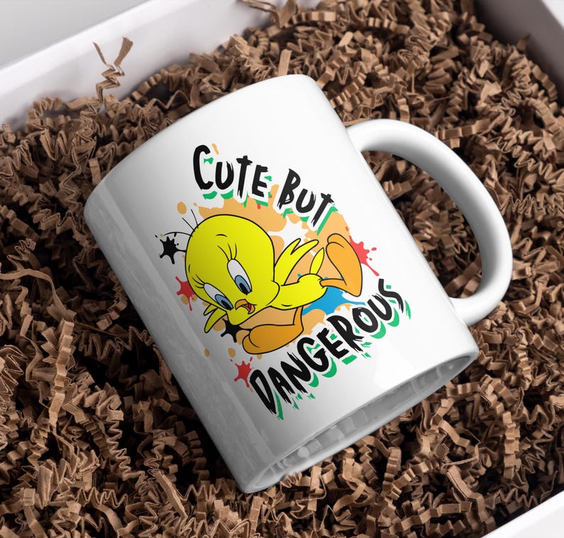 Puede incluir: Taza de cer&aacute;mica blanca con Tweety Bird y el texto "CUTE BUT DANGEROUS". El personaje de dibujos animados es amarillo con ojos azules y pies naranjas. La taza est&aacute; dentro de una caja blanca llena de material de embalaje marr&oacute;n.