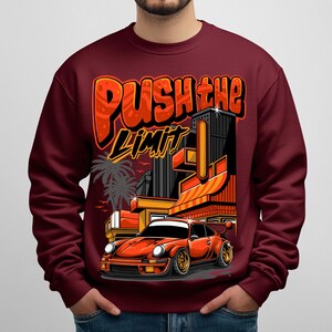 Puede incluir: Sudadera burdeos con un dise&ntilde;o gr&aacute;fico que presenta un coche deportivo naranja, edificios de la ciudad y el texto "PUSH THE LIMIT" en naranja y negro. El dise&ntilde;o tiene un estilo retro y urbano.