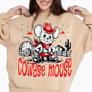 Puede incluir: Sudadera beige con un ratón de dibujos animados vestido de vaquero, con sombrero y pañuelo rojos. El diseño incluye el texto "COWYSE MOUSE" en rojo, junto con una escena rural con un cactus y una valla de madera.