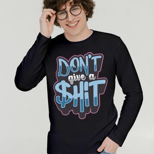 May include: Black long-sleeve shirt with the text "DON'T give a $HIT" in blue and pink lettering. The shirt has a crew neck and is made of a soft material. The graphic design is centered on the front of the shirt.