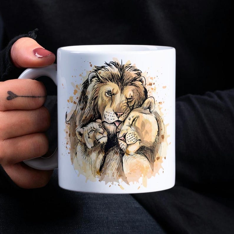 Puede incluir: Taza de cer&aacute;mica blanca con una ilustraci&oacute;n de acuarela de una familia de leones. El le&oacute;n, la leona y el cachorro est&aacute;n representados en un abrazo cari&ntilde;oso, con la leona descansando su cabeza en la espalda del le&oacute;n. La ilustraci&oacute;n est&aacute; rodeada de un fondo de acuarela marr&oacute;n claro.